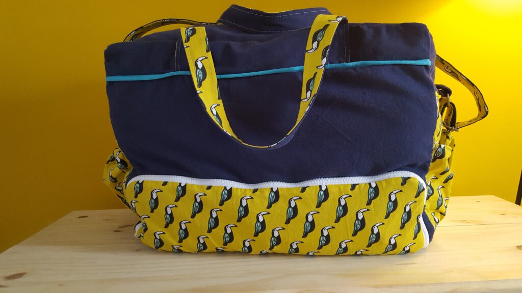 photo d'un sac à langer cousu à la main. tissu bleu marine et jaune avec des toucans