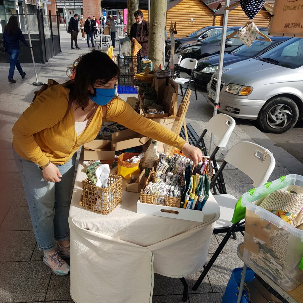 Photo d'une femme portant un masque installe son stand de créations textiles sur un marché artisanal (photo nouveau blog la sardine verte)