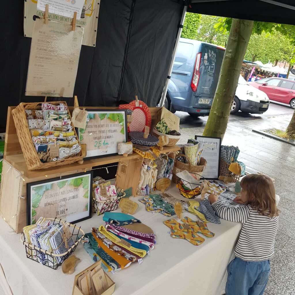 photo d'un stand de marché artisanal: des créations zéro déchet sont installées sur une table. Un enfant fait du coloriage 