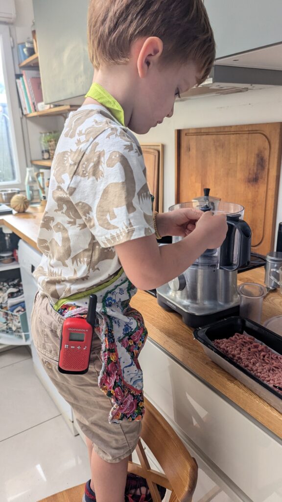 Enfant debout sur une marche qui prépare de la viande dans une cuisine