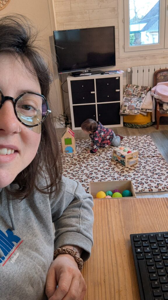 Photo d'une maman travaillant sur son ordinateur pendant que son bébé joue sur son tapis avec ses jouets.