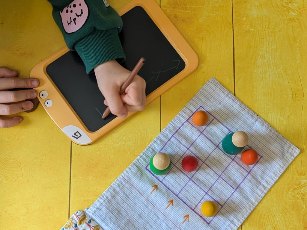 idée facile d'activité enfants : photo d'un enfant qui trace des flèches sur une ardoise pour indiquer le chemin que doit emprunter le personnage pour rejoindre l'autre